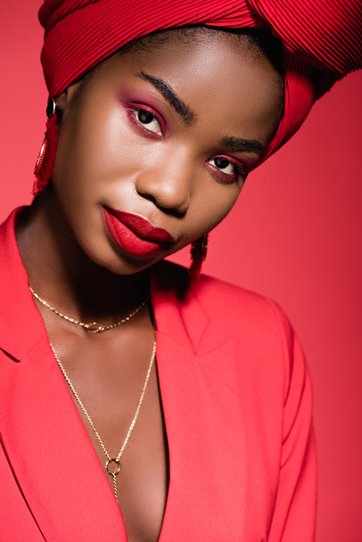 african american young woman in stylish outfit and turban isolated on red - Fotó, kép
