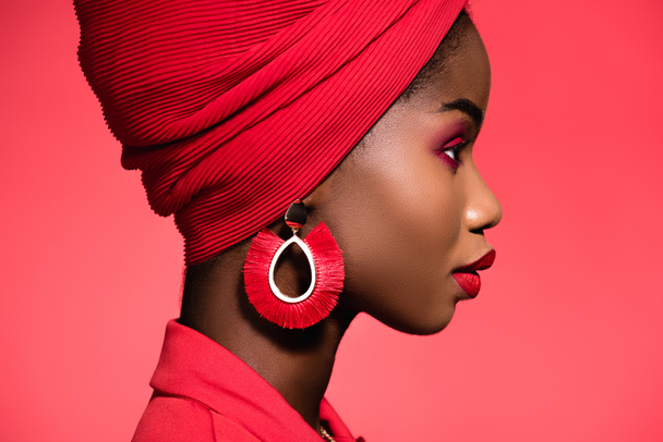 profil de la jeune femme afro-américaine en tenue élégante et turban isolé sur rouge - Photo, image
