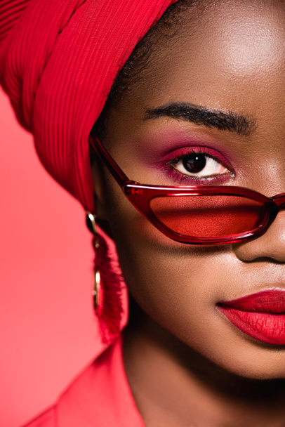 gros plan de afro-américaine jeune femme en lunettes de soleil et turban isolé sur rouge - Photo, image