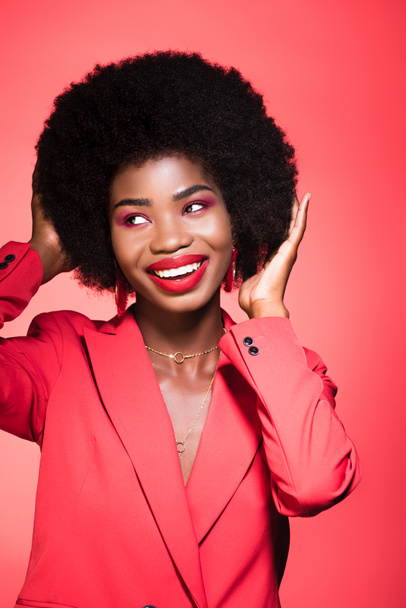 feliz afroamericana joven mujer en elegante traje aislado en rojo - Foto, Imagen