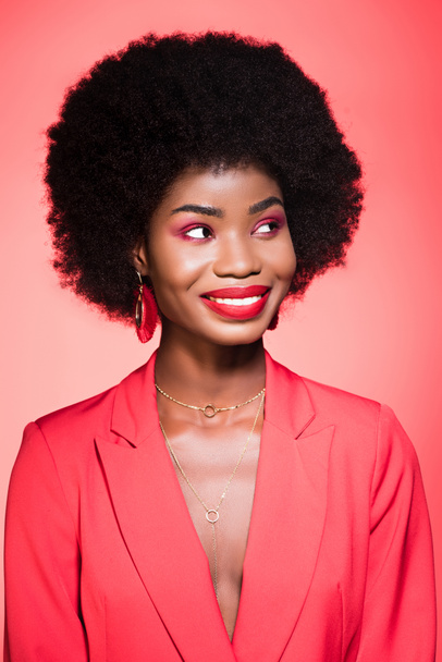 gelukkig Afrikaans amerikaans jong vrouw in stijlvolle outfit geïsoleerd op rood - Foto, afbeelding