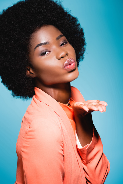 afro americano jovem mulher no laranja elegante roupa soprando beijo isolado no azul - Foto, Imagem