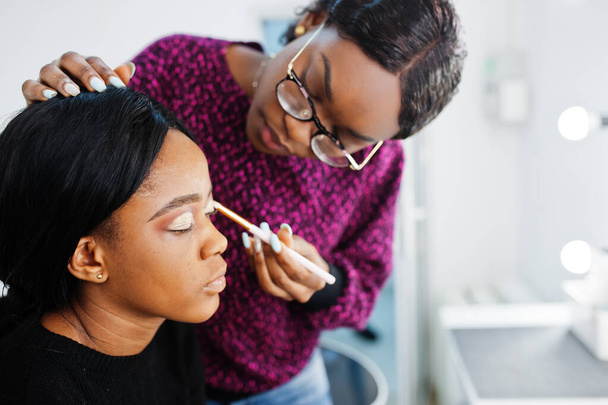 African American woman applying make-up by make-up artist at beauty saloon. - Foto, imagen