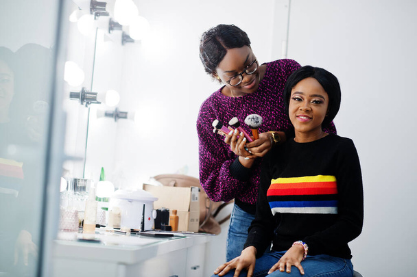 African American woman applying make-up by make-up artist at beauty saloon. - Foto, afbeelding