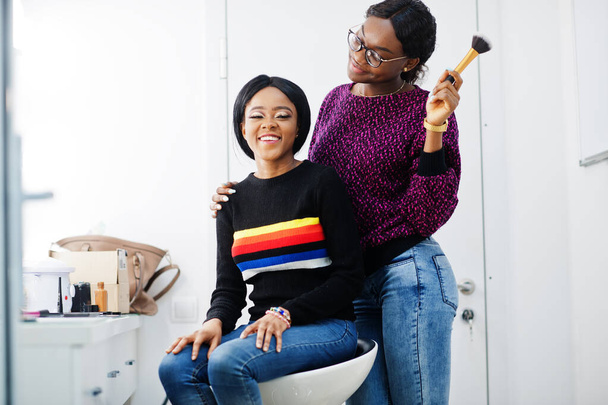 African American woman applying make-up by make-up artist at beauty saloon. - 写真・画像