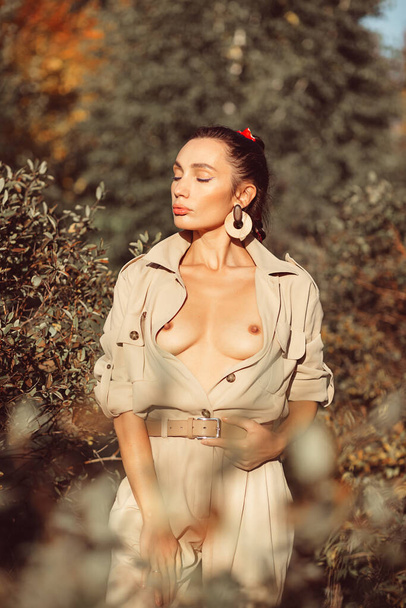 Young beautiful brunette girl with good makeup on her face with expressive features and figure. in autumn among beautiful trees, she is wearing a stylish suit - Fotó, kép