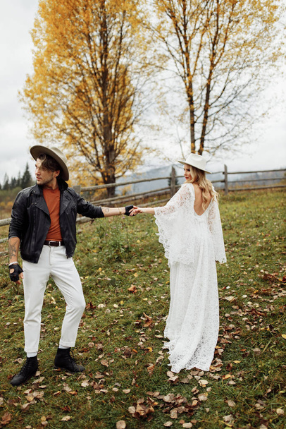Beautiful couple walking at the field, attractive woman hold a hand of handsome man, adorable wife look at charming husband, enjoy spend time together, stylish photoshoot concept. High quality photo - Foto, Bild