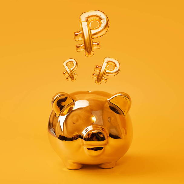 Salvadanaio dorato su sfondo giallo con Golden Ruble Sign Balloons. Simbolo di valuta russa realizzato in palloncino di alluminio. Concetto di investimento e bancario. Risparmio di denaro, cassa, finanza, investimenti. - Foto, immagini