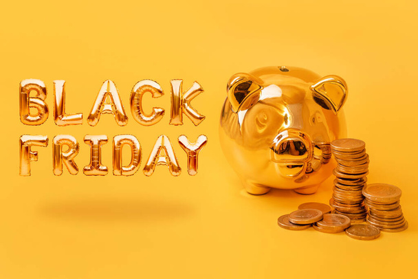 Golden piggy bank with money towers on yellow background with text Black Friday. Stack of euro coins near golden money box. Money pig, money saving, moneybox, sale and discount concept - Photo, Image