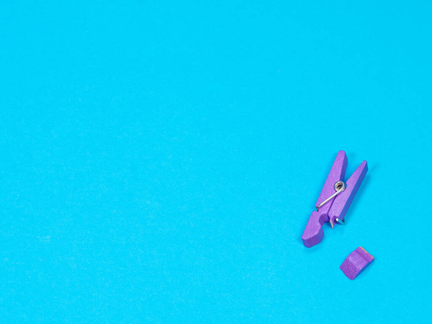 Spring-type wooden violet clothespin with fracture leg on blue background - Photo, Image