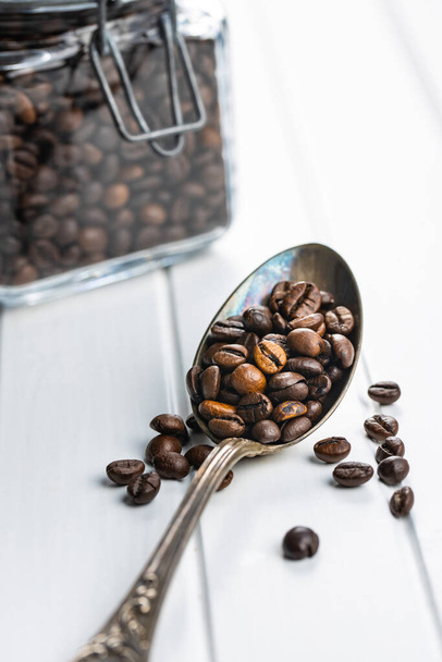 Roasted coffee beans in spoon on white table. - Foto, Bild