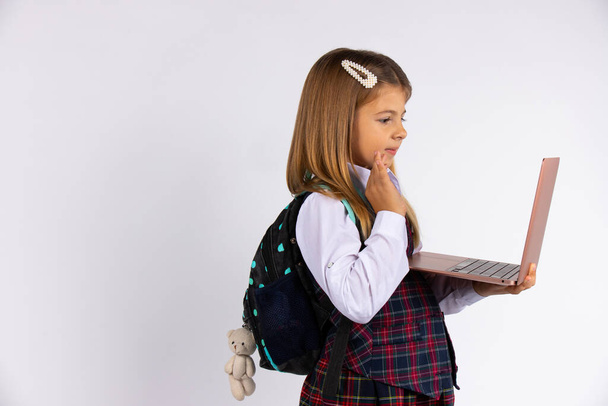 Cute little girl in school uniform holding a laptop computer showing hello isolated on gray background. Online learning concept. - Photo, Image