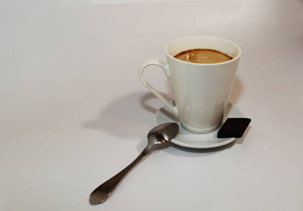 Coffee latte in a white mug and a slice of chocolate on a gray background. - Photo, Image