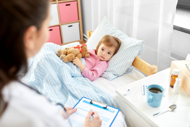 doctor with clipboard and sick girl in bed at home - Foto, Imagem