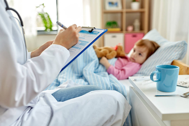 doctor with clipboard and sick girl in bed at home - Foto, Imagem