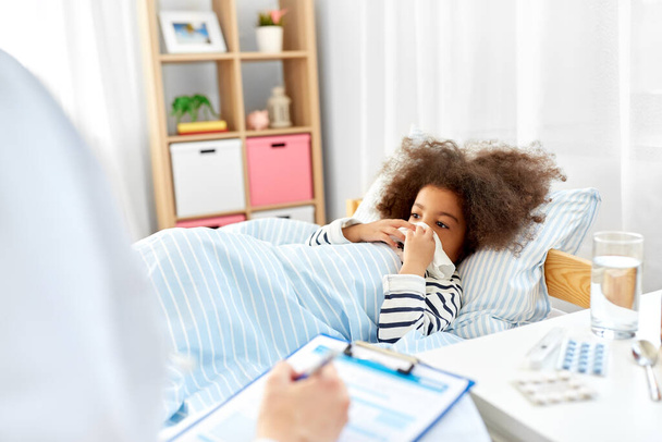 doctor with clipboard and sick girl in bed at home - Foto, Bild
