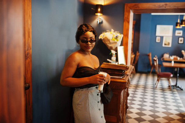 Portrait of african american woman, retro hairstyle posing at restaurant with cup of latte. - 写真・画像