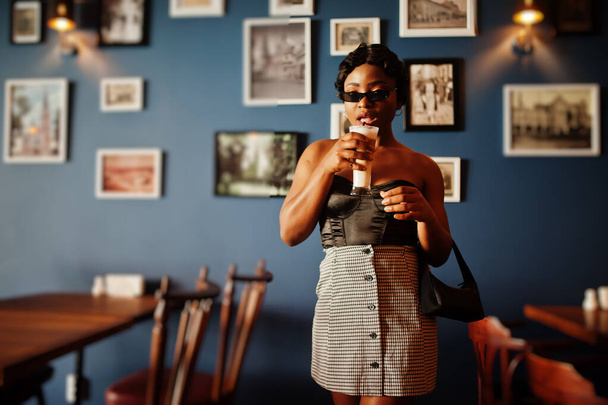 Retrato de mujer afroamericana, peinado retro posando en restaurante con taza de café con leche. - Foto, imagen