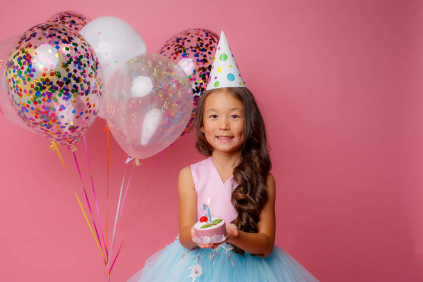 A young Asian girl blows out a candle on a pink background at a birthday party - Фото, изображение