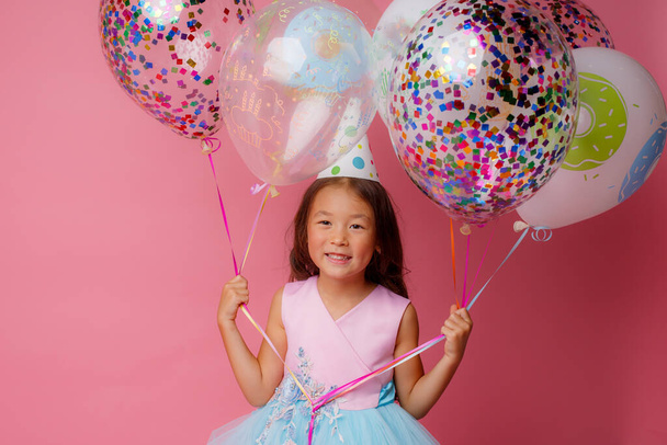 Una joven asiática en una fiesta de cumpleaños está jugando con globos sobre un fondo rosa - Foto, Imagen