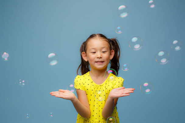 Азиатская девушка играет с мыльными пузырями в Студии на синем фоне - Фото, изображение