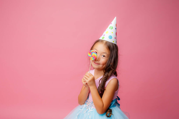 Young Asian girl at a birthday party with a Lollipop on a pink background - Foto, Imagem