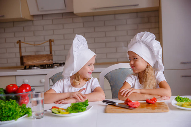 Két aranyos vicces lány pózol séf kalapban zöldségekkel az asztalon - Fotó, kép