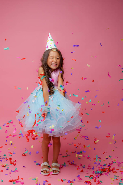 Азійська дівчинка святкує день народження, ловить конфетті на рожевому фоні - Фото, зображення