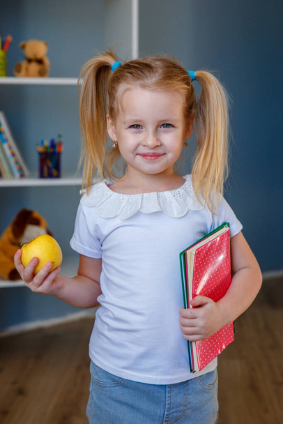 el concepto a la escuela de la educación. Una niña con un libro y una manzana en sus manos - Foto, imagen