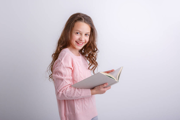 Дівчина-підліток з книгою в руках на сірому фоні
.   - Фото, зображення