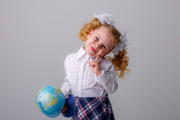 милая маленькая школьница держит глобус позируя в студии против серого - Фото, изображение