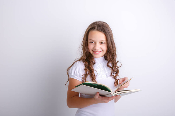 Ένα έφηβο κορίτσι με ένα βιβλίο στα χέρια της να ποζάρει στο στούντιο. - Φωτογραφία, εικόνα
