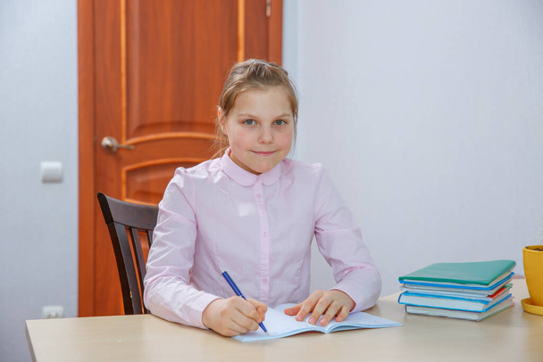 schoolgirl sitting at the table and writing homework  - Fotó, kép
