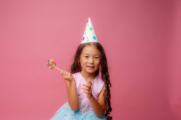 Young Asian girl at a birthday party with a Lollipop on a pink background - Foto, immagini