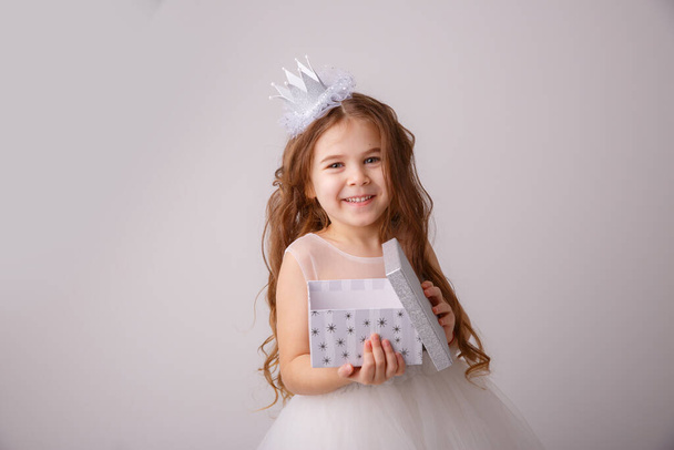 een klein meisje in een sprookjeskostuum, een prinses meisje met een geschenk in haar handen glimlachend, geïsoleerd op een witte achtergrond - Foto, afbeelding