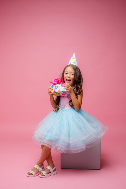 a little girl of Asian appearance holds a gift in her hands celebrating her birthday on a pink background - 写真・画像