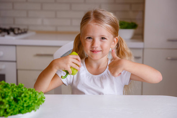 holčička blondýnka drží prst v kuchyni se zeleninou, - Fotografie, Obrázek