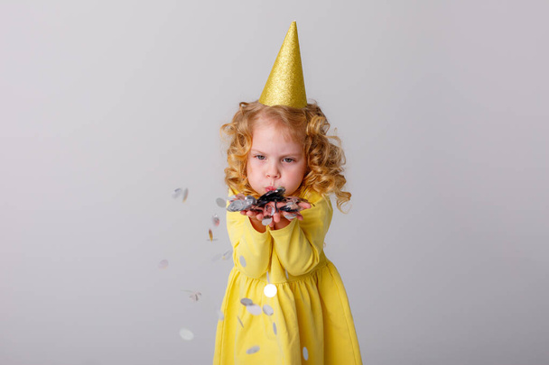 petite fille dans une robe jaune attrapant confettis sur fond gris - Photo, image