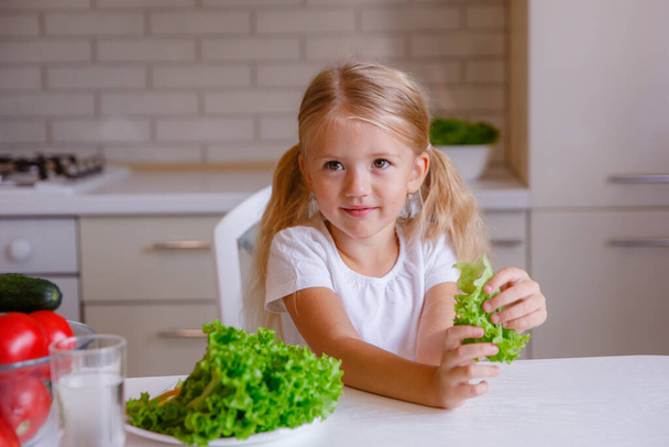 blonde baby girl eating vegetables in the kitchen - 写真・画像