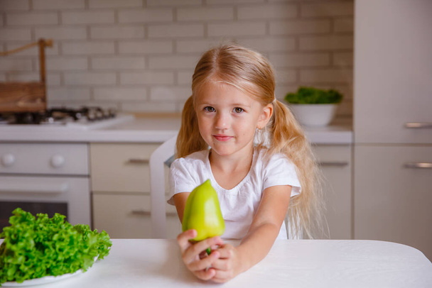 blond baby meisje eten groenten in de keuken - Foto, afbeelding