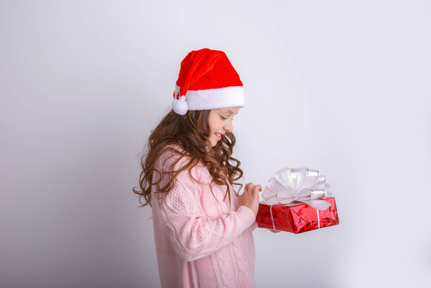 uśmiechnięta dziewczynka w kapeluszu Santa otwiera prezent w dłoni na odizolowanym białym tle - Zdjęcie, obraz