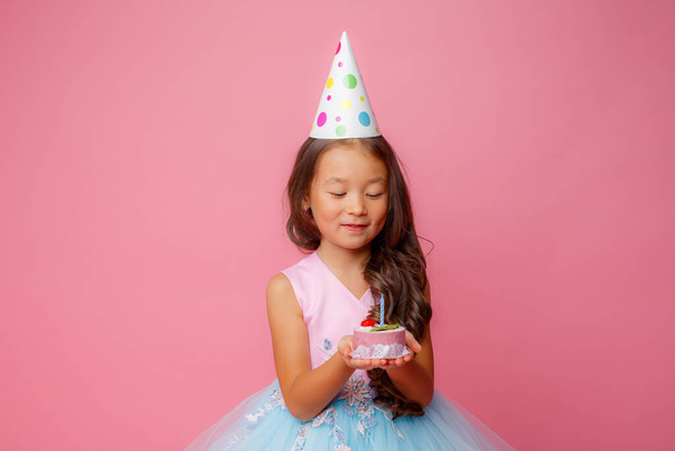 Młoda Azjatka na przyjęciu urodzinowym trzyma tort ze świecą na różowym tle - Zdjęcie, obraz
