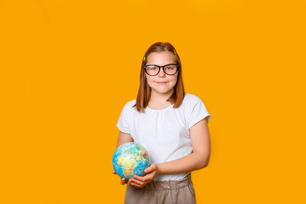 egy szemüveges iskolás lány egy földgömböt tart a kezében a Stúdióban narancssárga alapon. - Fotó, kép