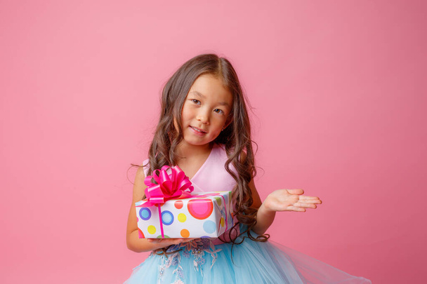 a little girl of Asian appearance holds a gift in her hands celebrating her birthday on a pink background - Valokuva, kuva