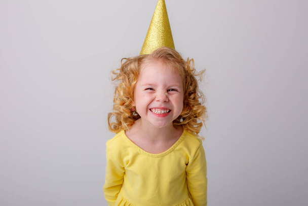 gelukkig meisje dragen gele jurk en verjaardag hoed - Foto, afbeelding