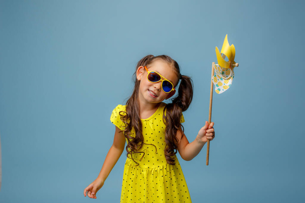 a little Asian girl with long hair holds a windmill toy smiling Studio on a blue background - Zdjęcie, obraz