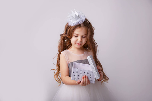 malá holčička v pohádkovém kostýmu, princezna dívka s dárkem v rukou s úsměvem, izolovaná na bílém pozadí - Fotografie, Obrázek