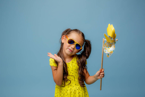 una piccola ragazza asiatica con i capelli lunghi tiene un giocattolo del mulino a vento sorridente Studio su uno sfondo blu - Foto, immagini