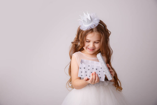 Peri kostümü giymiş küçük bir kız, elinde bir hediyeyle beyaz bir arka planda soyutlanmış, gülümseyen bir prenses kız. - Fotoğraf, Görsel