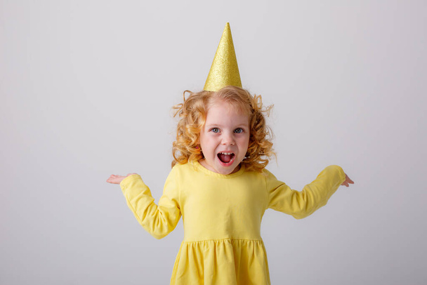 Kislány sárga ruhában, szülinapi kalapban, pózol a stúdióban. - Fotó, kép